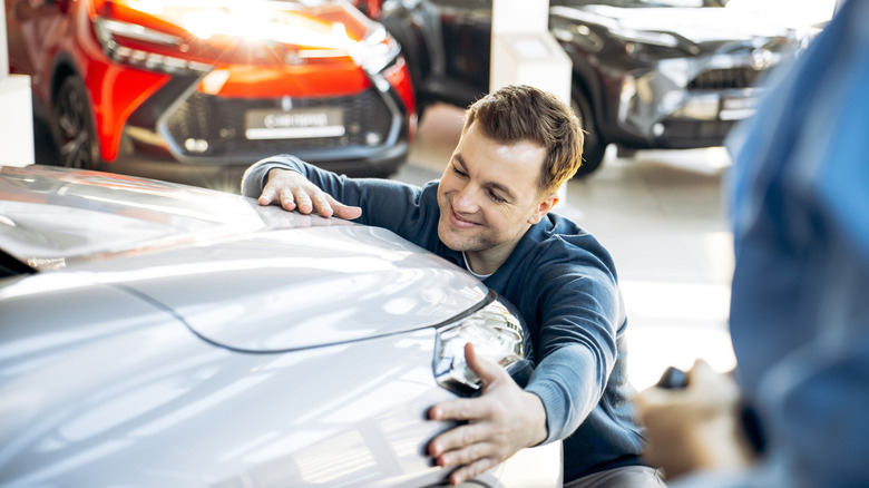 Ein Mann umarmt die Vorderseite eines Autos im Ausstellungsraum eines Autohauses