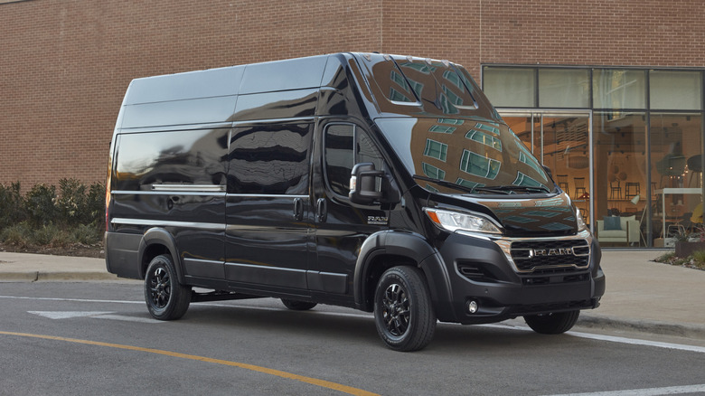 Vordere 3/4-Ansicht eines verdunkelten 2025 Ram ProMaster auf einer Straße mit einem Backsteingebäude im Hintergrund