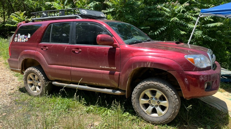 Seitenansicht eines roten Toyota 4Runner aus dem Jahr 2006, der im Gras geparkt ist, mit Bäumen dahinter
