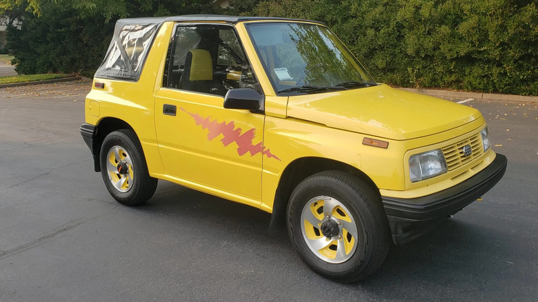 Eine Dreiviertelaufnahme von vorne eines gelben Geo Tracker-Verdecks, das auf Asphalt vor einer Hecke geparkt ist
