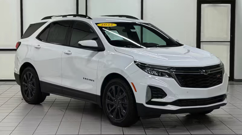 Ein weißer Chevrolet Equinox mit schwarzen Rädern auf einem Fliesenboden und einer weißen Wand mit Metallstangen.