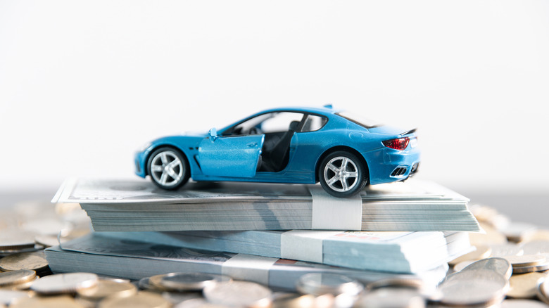 Ein blaues Ford Mustang-Modellauto steht auf einem Stapel Geld und Münzen.