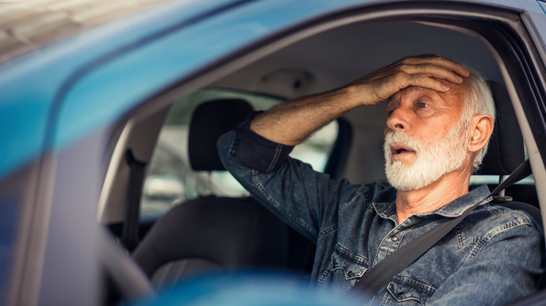 Ein älterer Mann hinter dem Steuer eines Autos mit der Handfläche auf der Stirn