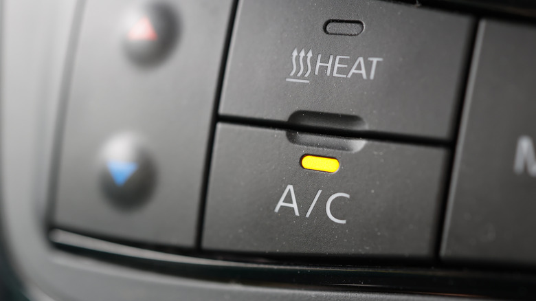 Nahaufnahme eines eingeschalteten AC-Knopfes am Armaturenbrett eines Autos