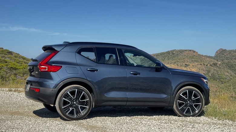 Eine Seitenansicht des blauen XC40, der auf Schotter geparkt ist, vor einer Aussicht auf strauchbedeckte Berge und einen blauen Himmel