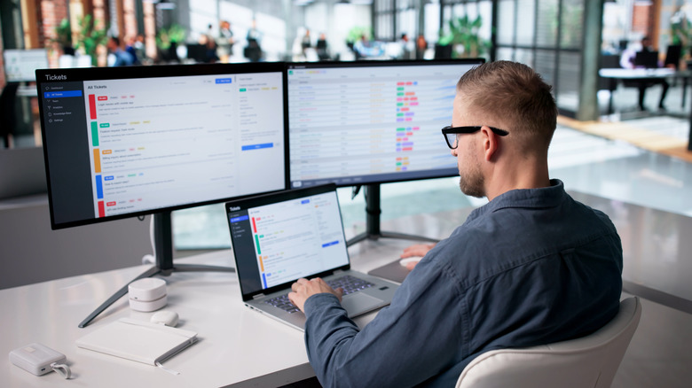 Ein Mann sitzt an einem Schreibtisch und betrachtet Daten auf mehreren Computerbildschirmen