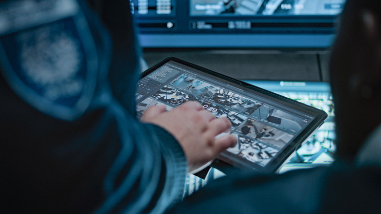 Ein Polizist schaut sich auf einem Tablet in einem Rechenzentrum das Video einer Überwachungskamera an