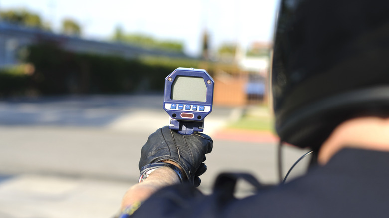 Eine Schulteraufnahme eines Polizisten mit einer Radarpistole, die tatsächlich abseits der Fahrbahn steht.