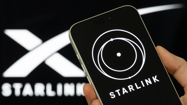 Eine Hand, die ein Telefon mit der Starlink-App auf dem Bildschirm hält, mit einem Starlink-Logo im Hintergrund