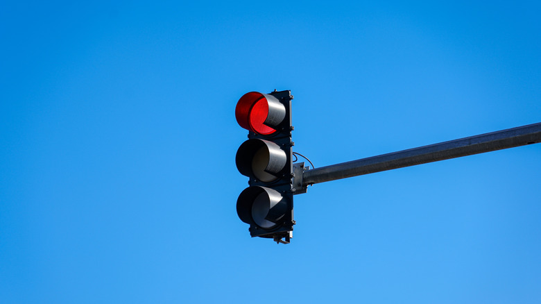 Eine schwarze Ampel zeigt ein rotes Licht vor blauem Himmel.