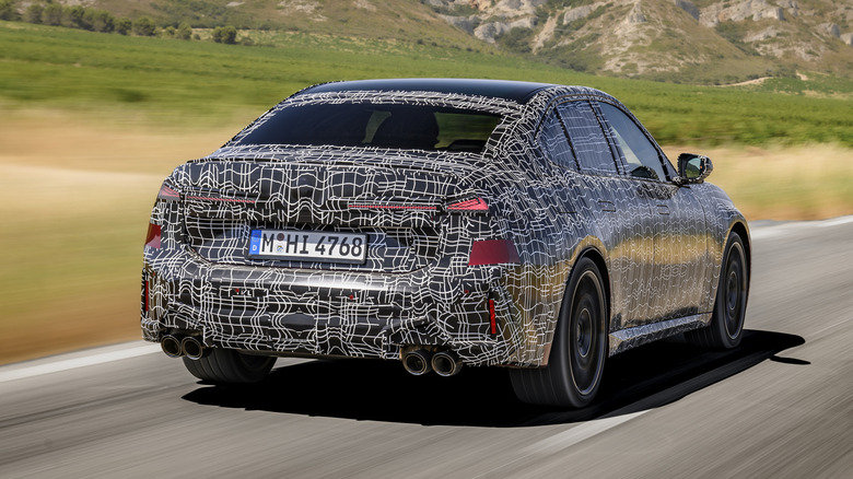 3/4-Hinteransicht des getarnten BMW M350 xDrive 2027 in Bewegung.