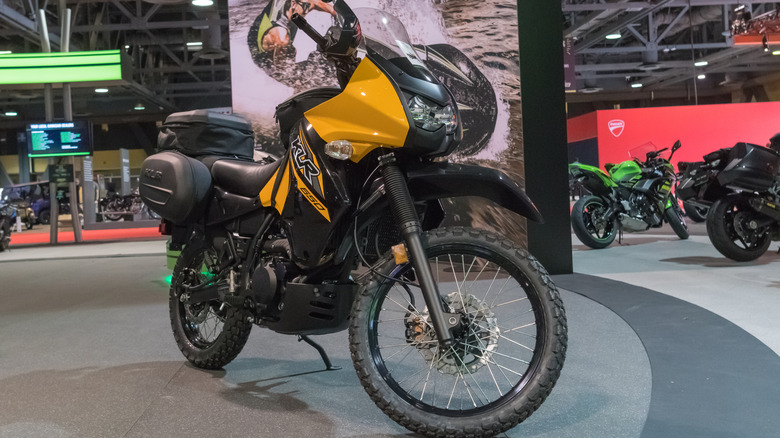 Eine neue schwarz-gelbe Kawasaki KLR 650 auf einem Messestand mit verschiedenen anderen Motorrädern im Hintergrund