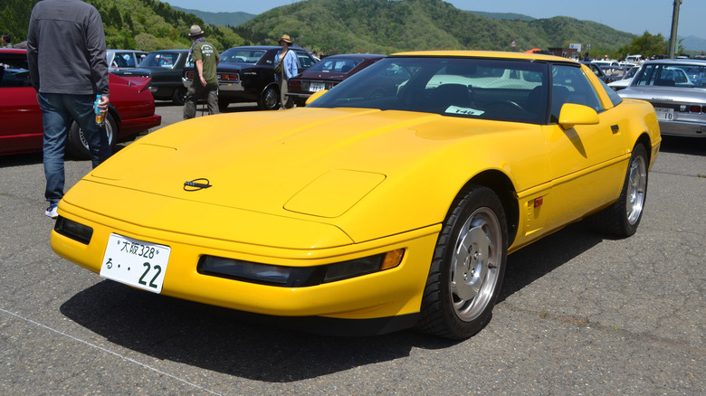 3/4-Ansicht von vorne links einer gelben C4 Corvette, die auf einer gepflasterten Fläche geparkt ist, mit anderen Autos im Hintergrund