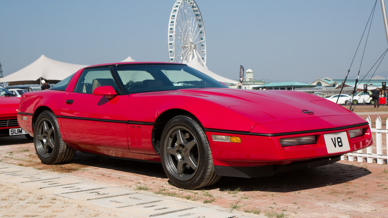 Eine rote Chevrolet Corvette der C4-Generation parkte vor einem weißen Lattenzaun mit einem Riesenrad im Hintergrund