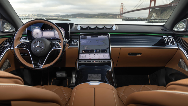 Eine Totalaufnahme des Armaturenbretts im Mercedes-Maybach S680 2026 mit dunkelbraunem Innenraum und Blick auf die Golden Gate Bridge durch die Windschutzscheibe an einem grauen Tag