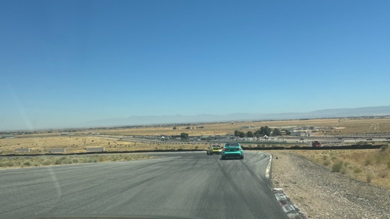 Eine Weitwinkelaufnahme vom Beifahrersitz aus zeigt einen türkisfarbenen M3, der einem gelben Textmarker folgt, mit der weiten Aussicht auf Willow Springs und die Wüste und einem klaren blauen Himmel