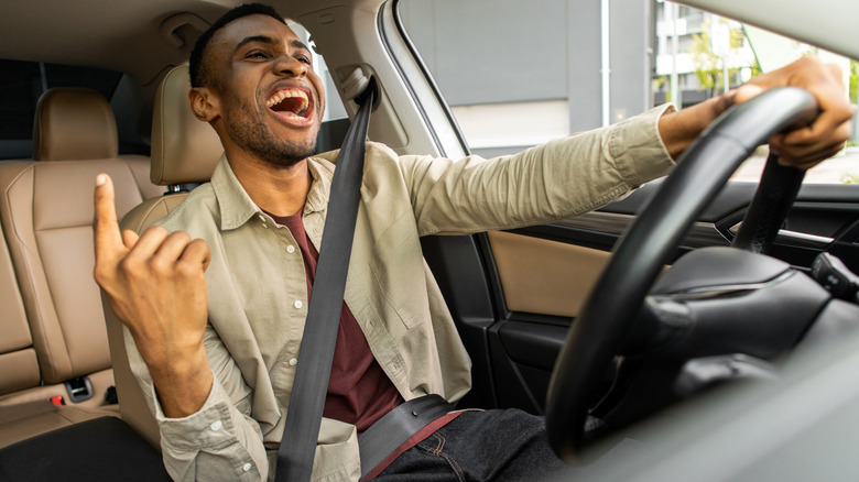 Fröhlicher schwarzer Mann tanzt im Auto und singt, während er sein Auto fährt. Fahrspaß