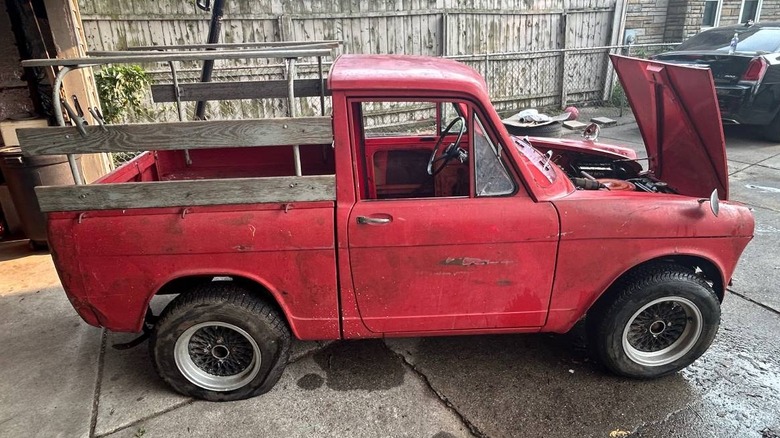 Ein roter Daihatsu Hijet Pickup mit hölzernen Seitengittern auf der Ladefläche und geöffneter Motorhaube, geparkt in einer Vorstadteinfahrt.