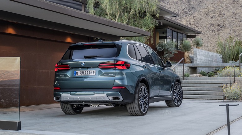 3/4-Hinteransicht eines 2024 BMW X5, der in der Einfahrt eines Hauses in der Wüste geparkt ist