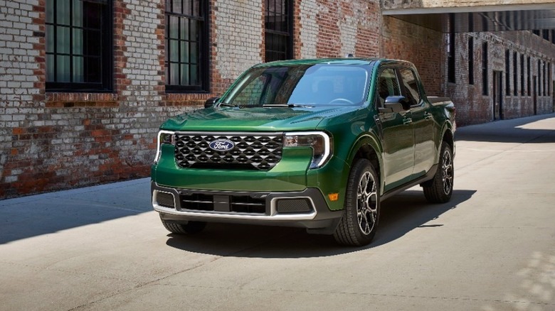 3/4-Vorderansicht eines grünen Ford Maverick Hybrid, der neben einem alten Backsteinfabrikgebäude geparkt ist