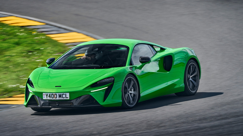 Vordere Dreiviertelaufnahme eines leuchtend grünen McLaren Artura, der auf einer Rennstrecke mit schwarz-gelben Bordsteinen und grünem Gras um eine Ecke fährt