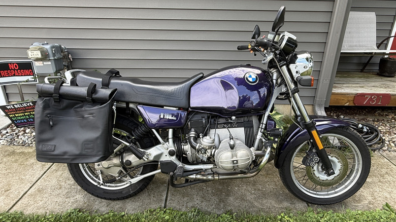 Eine lila BMW R100R von 1992 parkte auf dem Bürgersteig vor einem grauen Haus.
