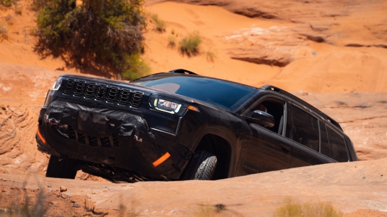 Ein schwarzer Cherokee Trailhawk fährt einen steilen Felshang hinauf, hinter dem ein Baum sichtbar ist
