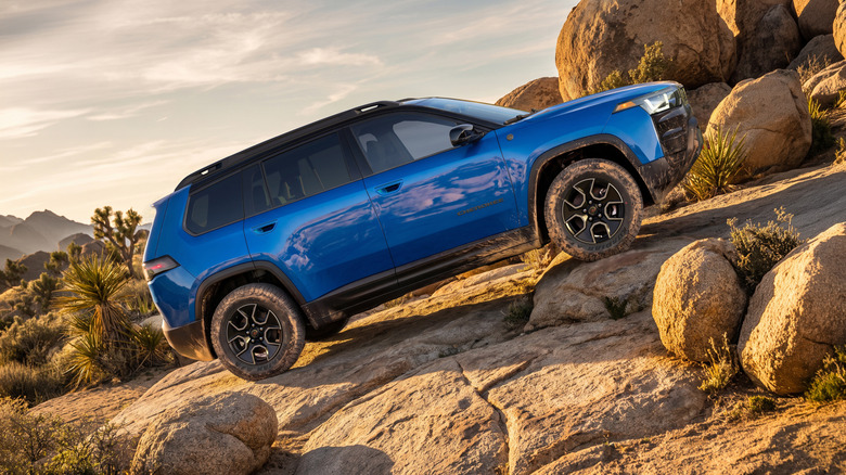Seitenansicht eines blauen Cherokee Trailhawk, der vor Joshua Trees und weiteren Felsen einen Felshang hinauffährt