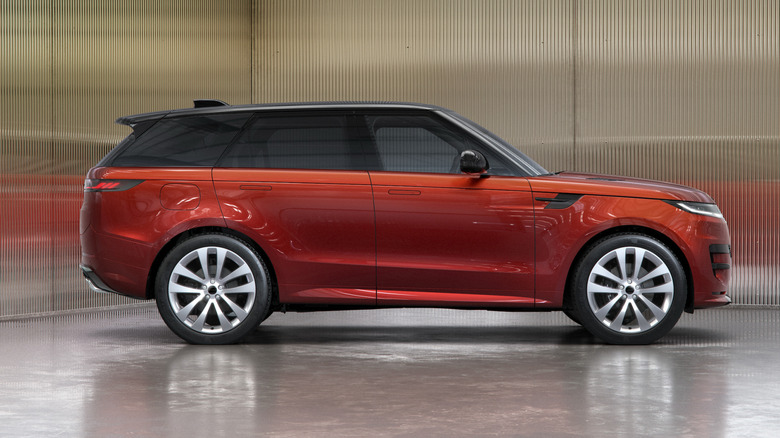 Seitenansicht eines roten Range Rover Sport, der auf einer unebenen Fläche vor reflektierenden Wellblechwänden geparkt ist