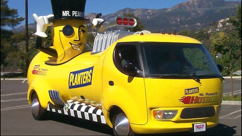 Eine Dreiviertel-Vorderansicht des NUTmobile Hot Rod von 1999, der auf einem Parkplatz vor Bergen geparkt ist