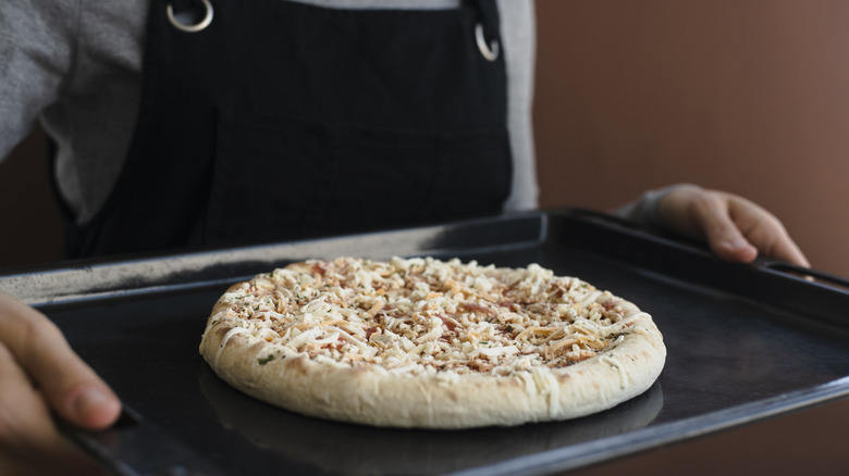 Eine gefrorene Pizza auf einem Backblech wird zum Ofen getragen