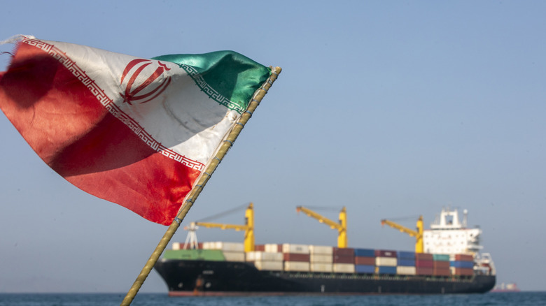 Eine iranische Flagge weht im Wind, während Schiffe am 16. Mai 2026 in der Straße von Hormus in der Nähe der iranischen Insel Larak vor Anker liegen.