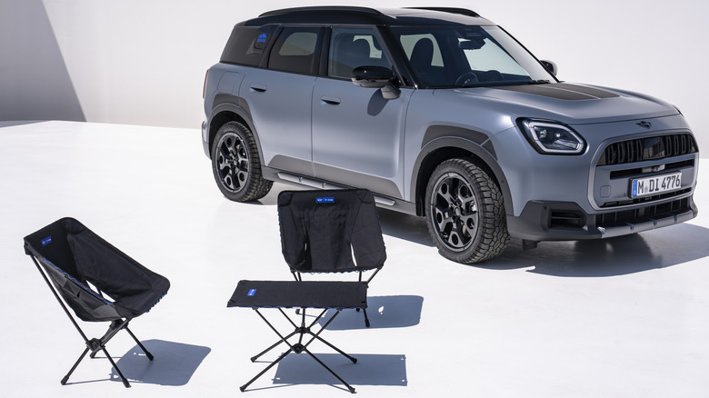 Ein mattblauer Countryman S Untamed Edition, geparkt auf einer weißen Fläche hinter der schwarzen faltbaren Campingausrüstung von Untamed