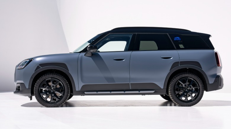 Seitenansicht eines mattblauen Countryman S Untamed, der auf einer weißen Fläche vor weißen Wänden geparkt ist