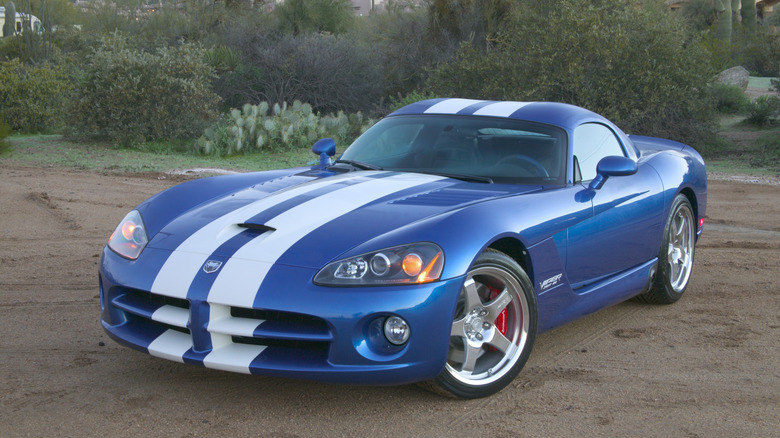 Vordere Dreiviertelaufnahme einer blauen SRT10 Viper mit weißen Streifen, die auf der Erde vor Sträuchern und Kakteen geparkt ist