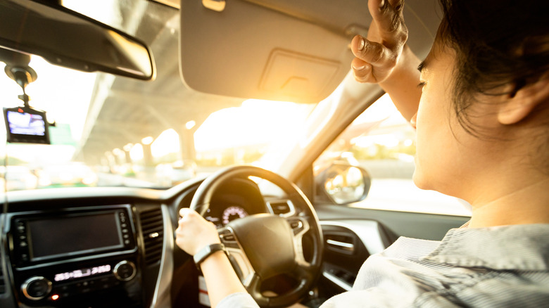 Eine Frau kämpft darum, sich vor der Abendsonne zu schützen, die sie blendet, während sie versucht, ihr Fahrzeug zu fahren.