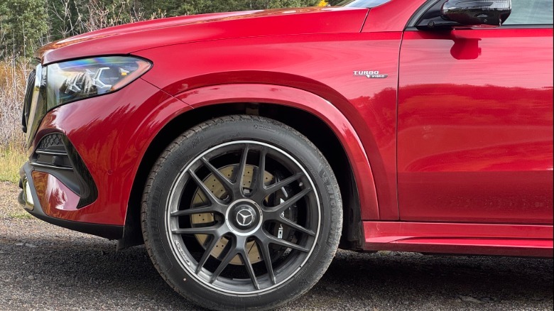 Eine Nahaufnahme der vorderen Seitenverkleidung und des schwarzen Rads des roten GLE53-Coupés, das auf Kies geparkt ist, mit einigen Bäumen und Büschen im Hintergrund