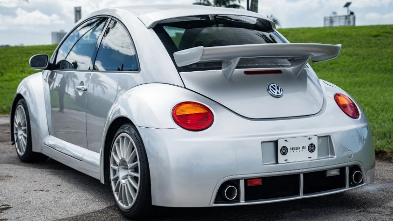 Hintere Dreiviertelaufnahme des silbernen Beetle RSi, der auf Asphalt vor grünem Gras und bewölktem Himmel geparkt ist