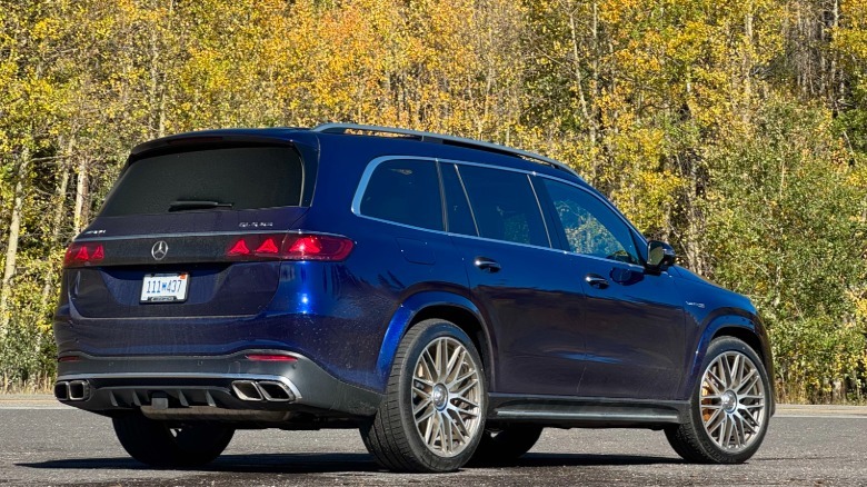 Eine Dreiviertelaufnahme von hinten von meinem dunkelblauen GLS63-Pressewagen, der auf Asphalt vor gelben und grünen Bäumen geparkt ist