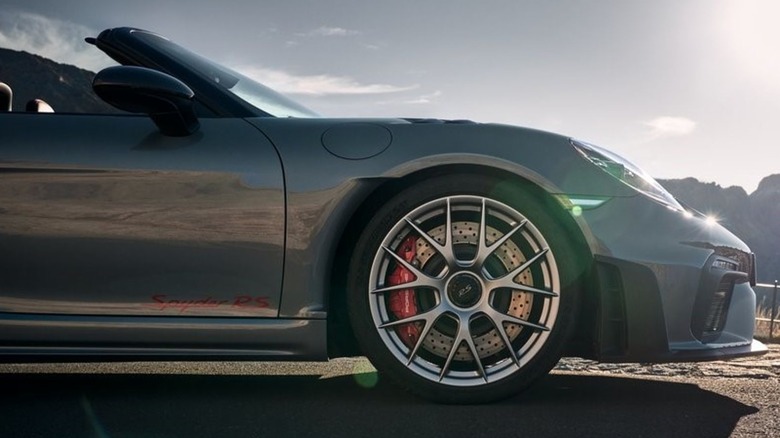 Nahaufnahme des Vorderrads eines grauen 718 Spyder RS, der vor einem teilweise bewölkten Himmel auf Asphalt geparkt ist