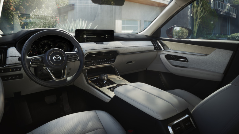 Das weiße Armaturenbrett eines CX-90 mit Pflanzen und einem Gebäude, das durch die Fenster sichtbar ist